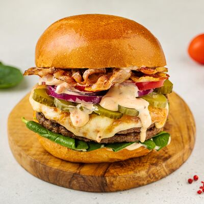 Бургер с двойной котлетой, жареным беконом, маринованным огурцом, красным луком и томатами в АндерСон по цене 1100 ₽